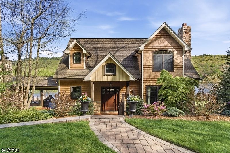 Front elevation of the cedar-shingled custom Colonial at 89 Woods Rd, with paver walkway, twin urn planters, dormer windows, and a stone-clad chimney