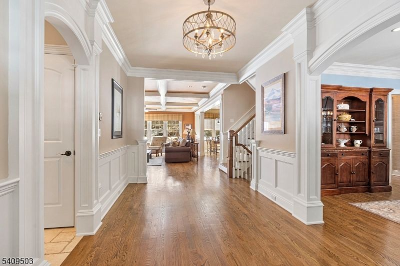 Entry foyer at 89 Woods Rd, with hardwood floors, wainscoting, an arched doorway to the dining room, and a chandelier over the central hall