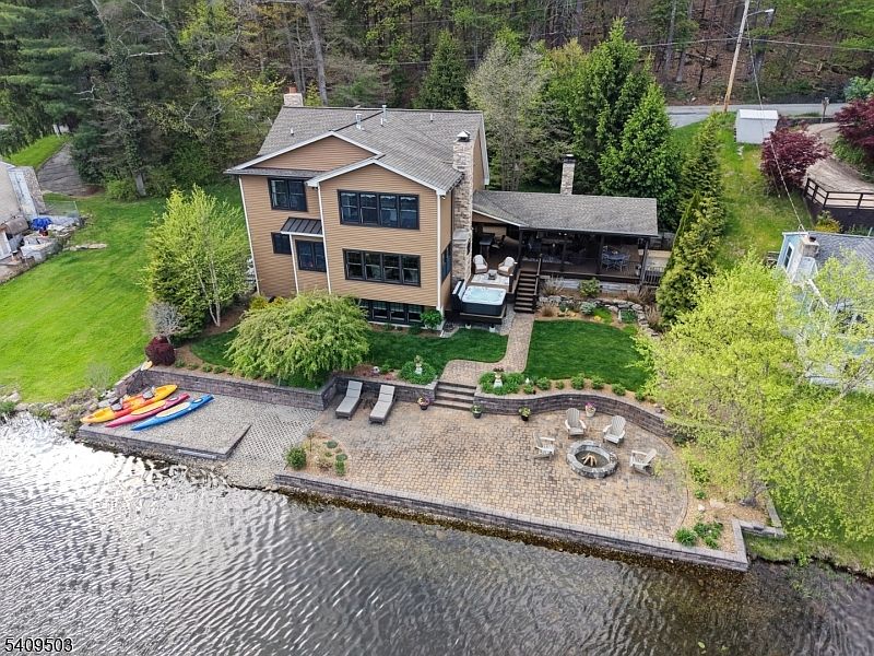 Aerial view of the custom Colonial lakehouse at 89 Woods Rd, with attached lakeside pavilion, paver patio, kayaks, and Kittatinny Lake at its doorstep